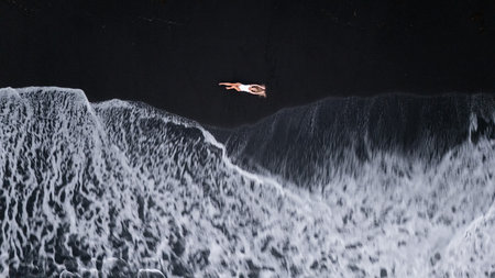 Top drone view of a woman lying on the black sand enjoying a moment waves