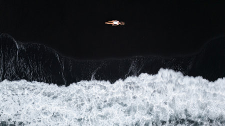 Top drone view of a woman lying on the black sand enjoying a moment waves