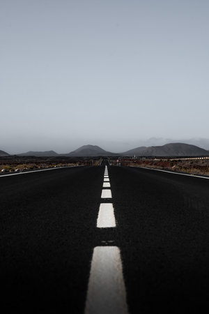 Vertical photo empty road stretches towards distant mountains under a calm skyの写真素材