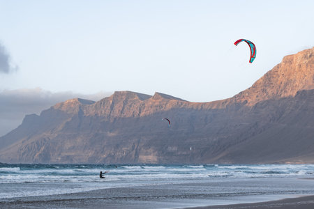 Kite surfer rides across waves at beach near the mountains in Famara, Lanzaroteの写真素材