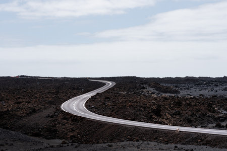 Curved road through volcanic landscape under cloudy sky in a remote areaの写真素材