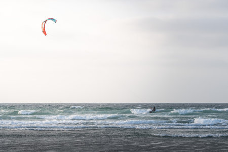 Kite surfer rides the waves at dawn on a coastline near mountainsの写真素材