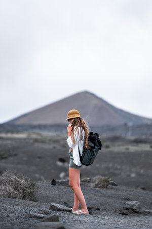 Hiker woman explores volcanic landscape near dormant mountain under cloudy skyの写真素材