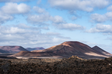 Timanfaya mountains and rolling hills bathed in sunlight under a cloudy skyの写真素材