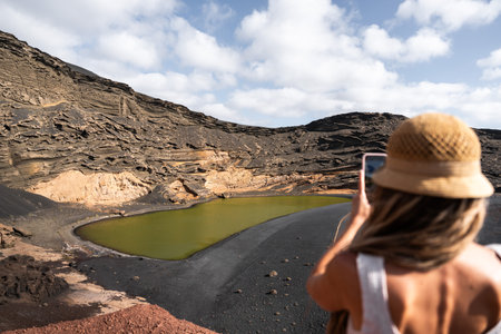 Woman takes a photo of the green lagoon charco in volcanic landscapeの写真素材