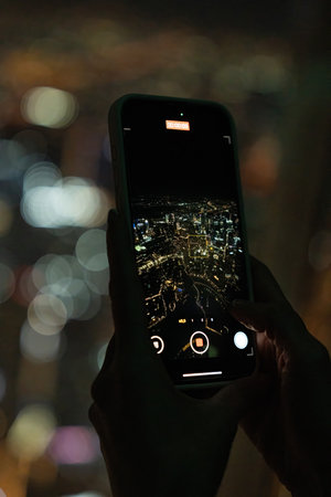 Tourist filming illuminated cityscape at night with smartphone from high vantage pointの写真素材