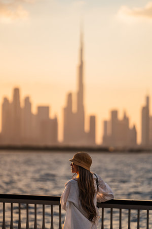 Tourist woman admiring dubai skyline at sunset from waterfront promenadeの写真素材