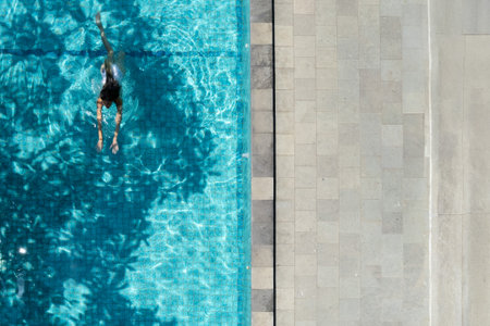 Woman swimming in turquoise pool with stone border, aerial view