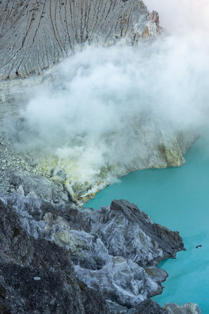 Kawah ijen volcano crater emitting sulfurous smoke and turquoise lakeの写真素材