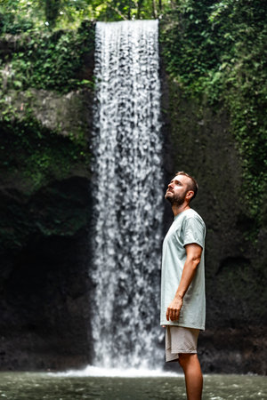 Tourist man enjoying the beauty of tibumana waterfall in baliの写真素材