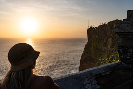 Tourist watching golden sunset over uluwatu temple, bali, indonesiaの写真素材