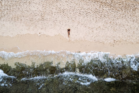 Aerial view of woman sunbathing on white sand beach with incoming wavesの写真素材