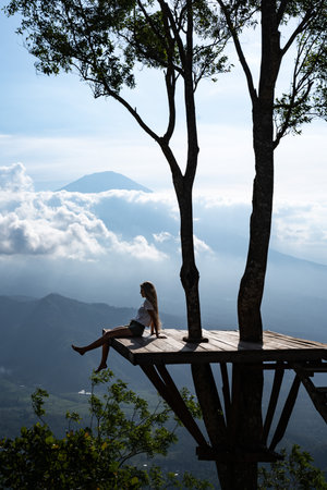 Tourist relaxing on a wooden platform enjoying view of mount agung volcano in bali, indonesia