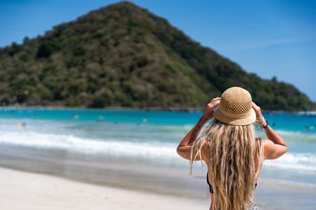 Tourist holding her straw hat looking at tropical beach and turquoise waterの写真素材