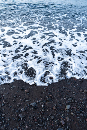 White sea foam washing over dark volcanic sand beachの写真素材