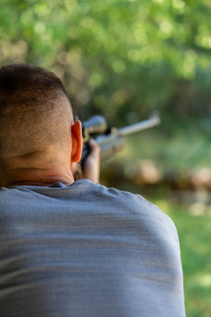 Back view man is holding a rifle and looking at something in the distance