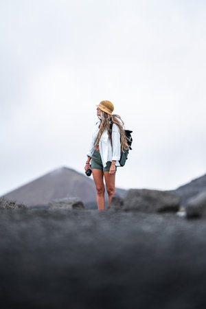 Woman exploring a volcanic landscape with a camera in hand during cloudy weatherの写真素材