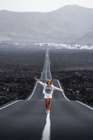 Woman walking joyfully on a long road in a volcanic landscape in Lanzarote