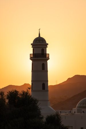 Oman mosque minaret silhouetted against desert sunset skyの写真素材