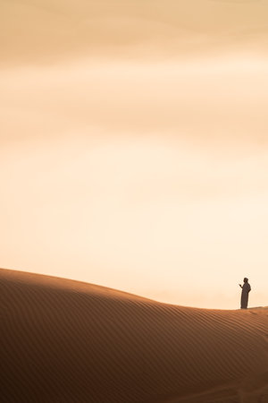 Unrecognizable man in traditional clothing standing on desert duneの写真素材