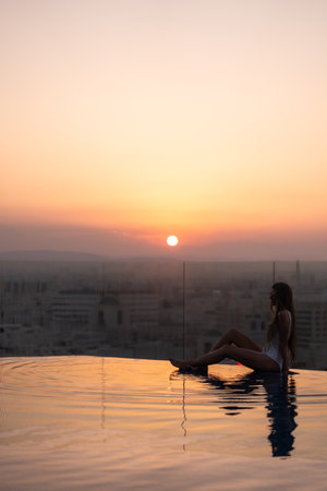 Woman relaxing at infinity pool at sunset overlooking cityの写真素材