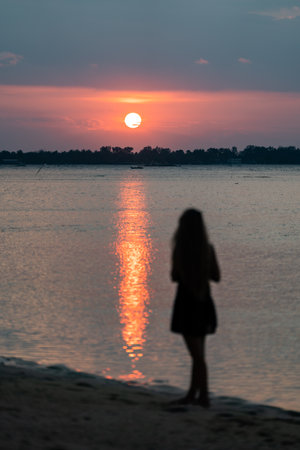 Woman contemplating sunset on beach enjoying solitudeの写真素材