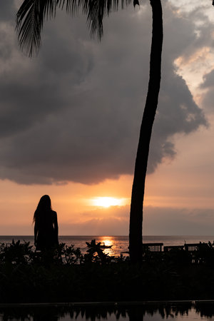 Woman enjoying tropical sunset reflecting on ocean waterの写真素材