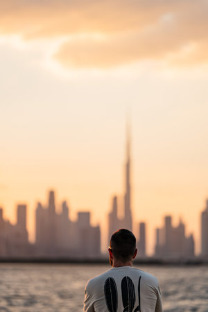 Tourist man admiring dubai skyline at sunset from the sea: burj khalifa in the backgroundの写真素材