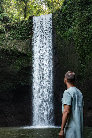 Tourist man admiring majestic waterfall in lush tropical rainforestの写真素材