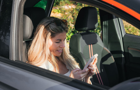 Blonde woman in copilot seat using a smart phone in car. Road trip, technology