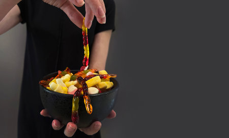 Treat or trick! Close up above top view cropped shot of woman holding and sharing black plate with colorful treats, unhealthy sweet candies. Halloween concept.の写真素材