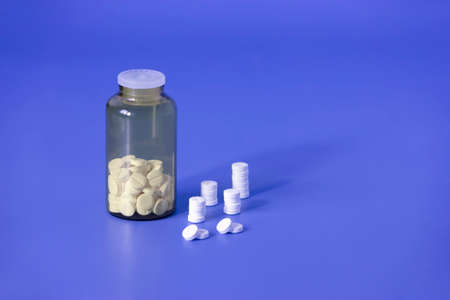 White pills, medical tablets, placebo or vitamins and brown transparent bottle with medicine on dark...