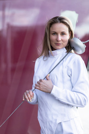 Portrait of white female fencer posing on red glass background, wears professional costume: white...