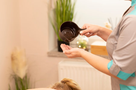Masseur pours warm melted lotion, oil from pottery on hand clbefore starting massage, kneading muscles of client in spa salon. Mental, health sustainability. Relaxation, healthcare.Horizontalの写真素材