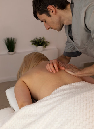 Male masseur, therapist stretches back of white woman, client during professional therapeutic massage in spa salon. Fascia stretching. Mental, health sustainability. Relaxation, healthcare. Verticalの写真素材