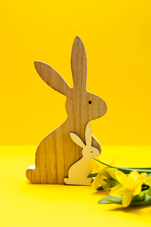 Wooden rabbit and bunny, yellow fresh narcissus flowers with green leaves on orange yellow background. Easter poster,celebration. Monochromatic greetings and present for Easter Day, vertical,copyspaceの写真素材