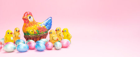Banner Chocolate chicken, hen with colorful bright sweet eggs wrapped in foil on festive Easter pink background. Confectionery, sweet-shop, candied children treat concept. Copy space,horizontalの写真素材
