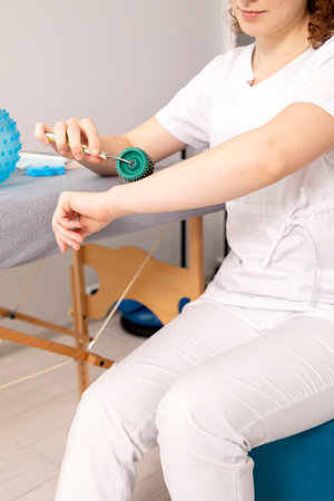 Rehabilitation Specialist, Physical Therapist Demonstrates Rehab Tool Meso Roller With Titanium Needles On Hand, Massage Ball With Pimples in Therapeutic Room. Healthcare, Rehabilitation. Verticalの写真素材