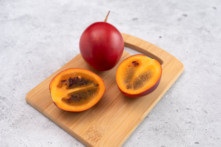 Fresh Exotic Fruit Tamarillo Sliced On Wooded Cutting Board On Table. Egg-shaped Edible Fruit Known As Tree Tomato, Plant Family Solanaceae, Solanum Betaceum. Top View. Flat Lay. Horizontal Planeの写真素材