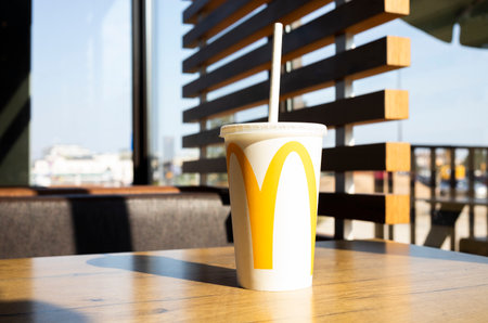 Refreshing McDonald Drink Milkshake In Big White Cup With Logo, Paper Straw on Table In Restaurant, McCafe. Hard Shadows Of Sun. Summer Beverage. Poland, Bialystok April 25, 2023 Horizontal planeのeditorial素材