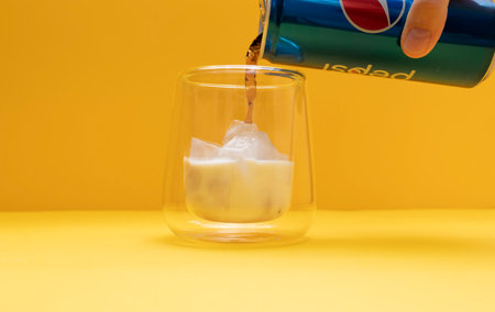 Someone cook Pilk, Trendy Pepsi Milk Drink. Person Combining soda and Dairy beverages. Drinking Glass With Ice, Milk, Filling with Pepsi On Yellow Background. Refreshment. Dirty soda. Horizontal Planeのeditorial素材