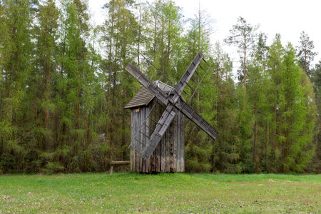 Old Wooden Mill In Meadow, Open Air. Blades Of Old Wooden Windmill In Rural Eastern Europe Area, Countryside. Green Forest On Background. Horizontal Landscape Plane High Quality Photoの写真素材