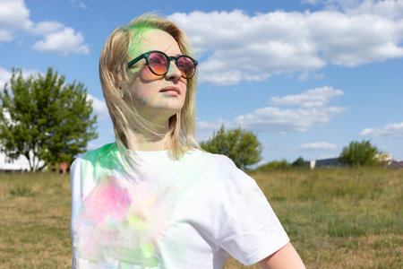 Portrait Beautiful White Blond Woman With Colored Dye, Powder On Face And Cloth On Holi Colors Festival In Meadow, Sunny Day. Playful Cultural Event With Throwing Bright Neon Powder. Horizontal Planeの写真素材