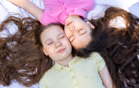 Top View Little Girls Lying On Plaid In Park, Meadow Under Sun, School Break Siblings Friendship, Having Fun In Nature. Horizontal Plane.の写真素材