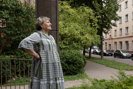 Real Smiling Female Woman In Yard Of Modern Building. Green Trees Around. Copy Space For Text. Pleased Elderly 70s Carefree, Full of Hope Beautiful Granny Looking Away Horizontal Plane.の写真素材