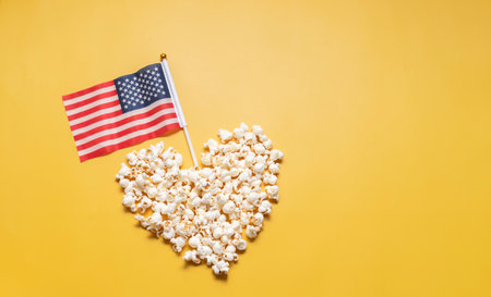 National Popcorn Lovers Day. Top View Popcorn in Heart Shape with American USA Flag on Yellow Background. Copy Space for Text. Greeting Card, Template No Text. Tasty salted Snack Flat Lay, Horizontalの写真素材