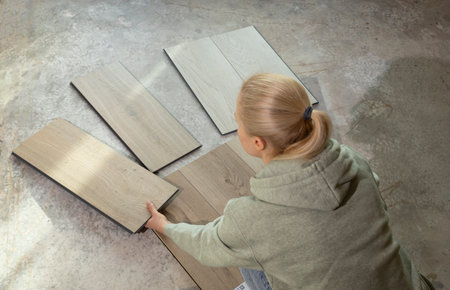 Woman Holds Luxury Vinyl Wood Samples On Concrete Floor In House. Choosing, Selecting Waterproof Flooring. Home Reconstruction. Vinyl Tiles Collection, Patterns. Interior Design Idea. Horizontal.の写真素材