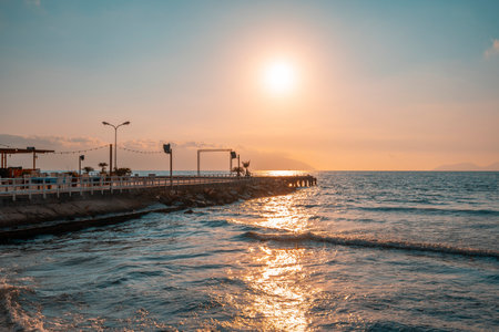 Sunset over the Mediterannean sea. Beautiful landscape of sandy beach with sea waves and wooden pier during sunset. Sky reflections in water.の写真素材