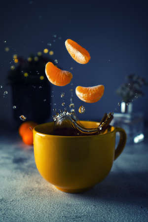 Tea splash composition on a dark blue background. Slices of mandarins are placed in splashes. Splashes of tea fly out of a cupの写真素材