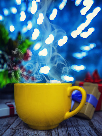 Orange cup of hot drink with a box of Christmas gifts and a Christmas tree. New Years holiday picture. Garlands in the backgroundの写真素材